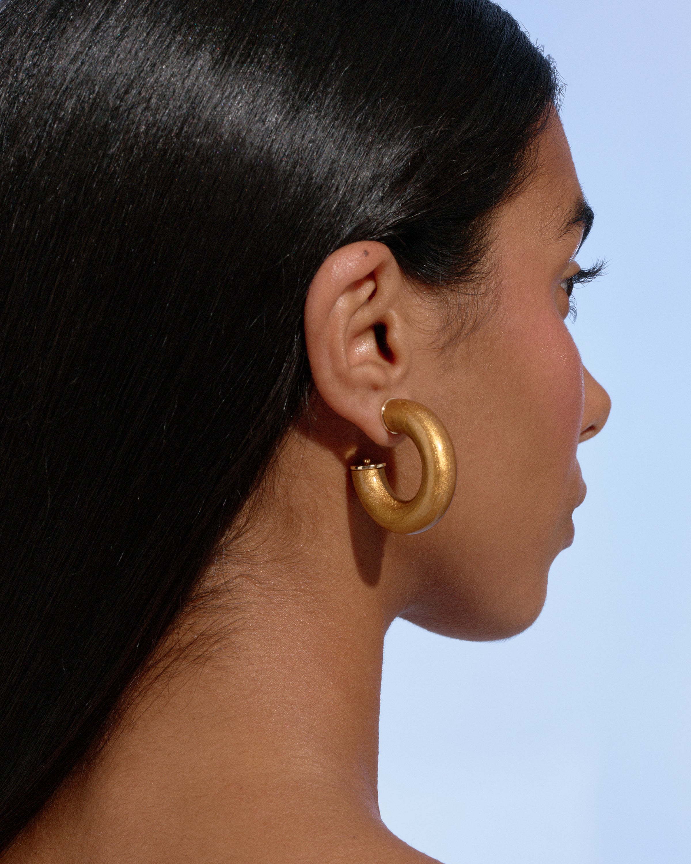 close-up side profile of a model wearing gold Alba Hoops against a soft blue background