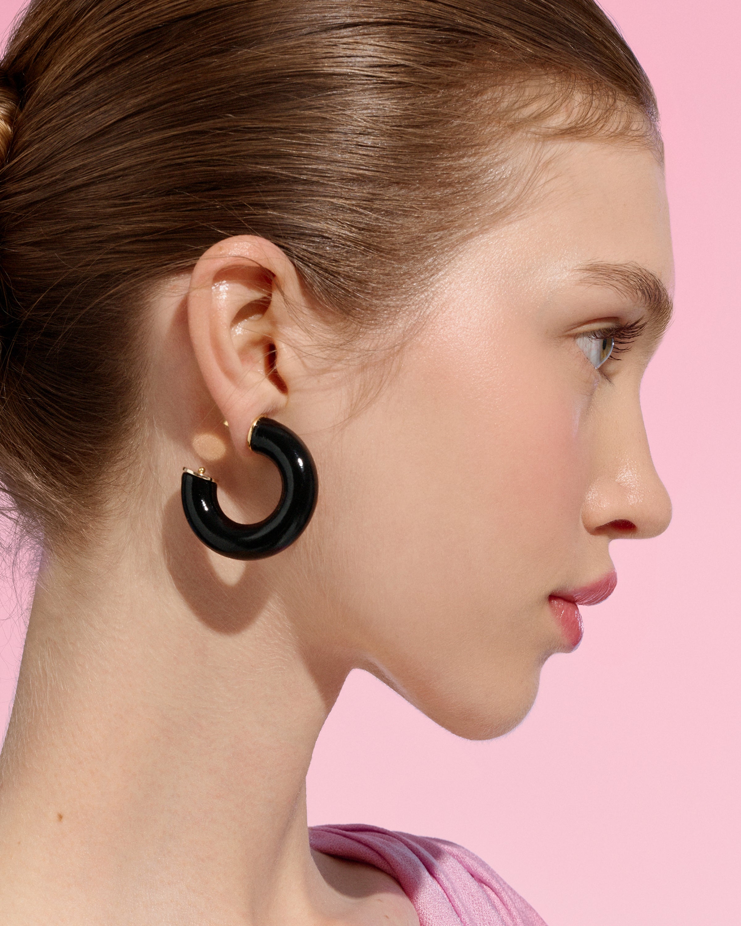side profile of a model wearing black Alba Hoops against a pink blue background
