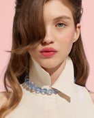Model wearing a blue beaded necklace against a pink background